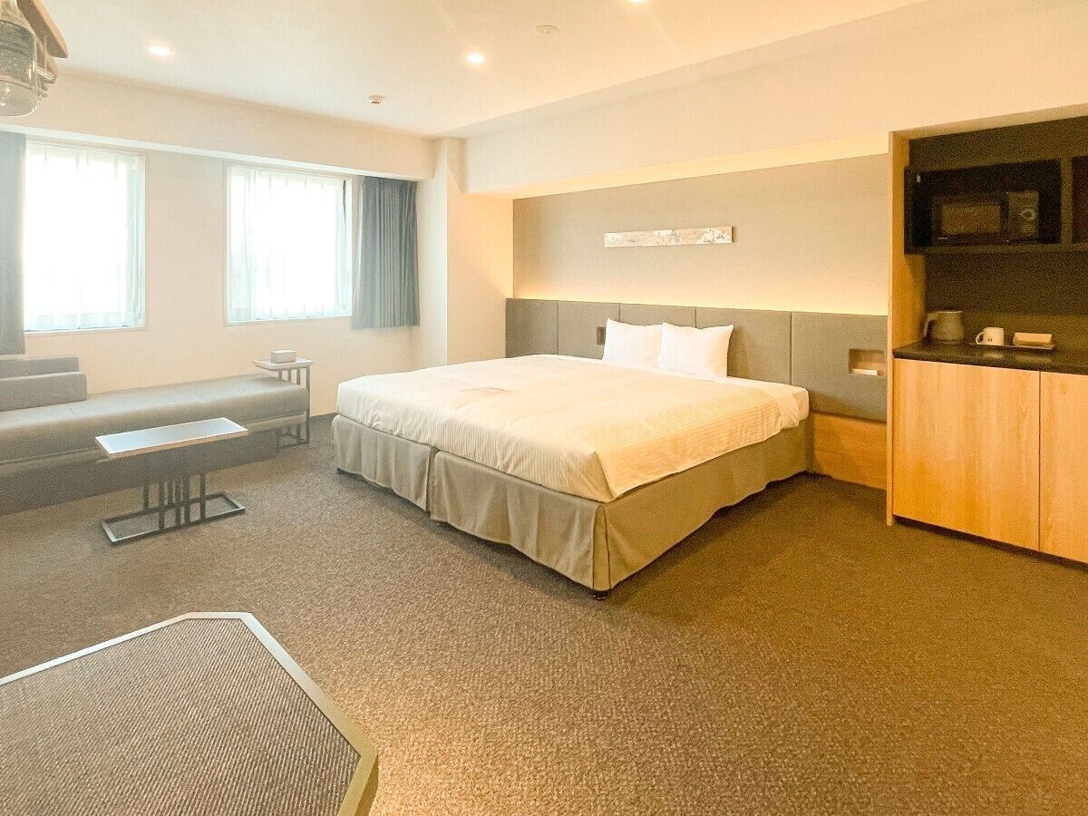 Quarto de hotel com cama, escrivaninha, cadeira, micro-ondas e cafeteira.