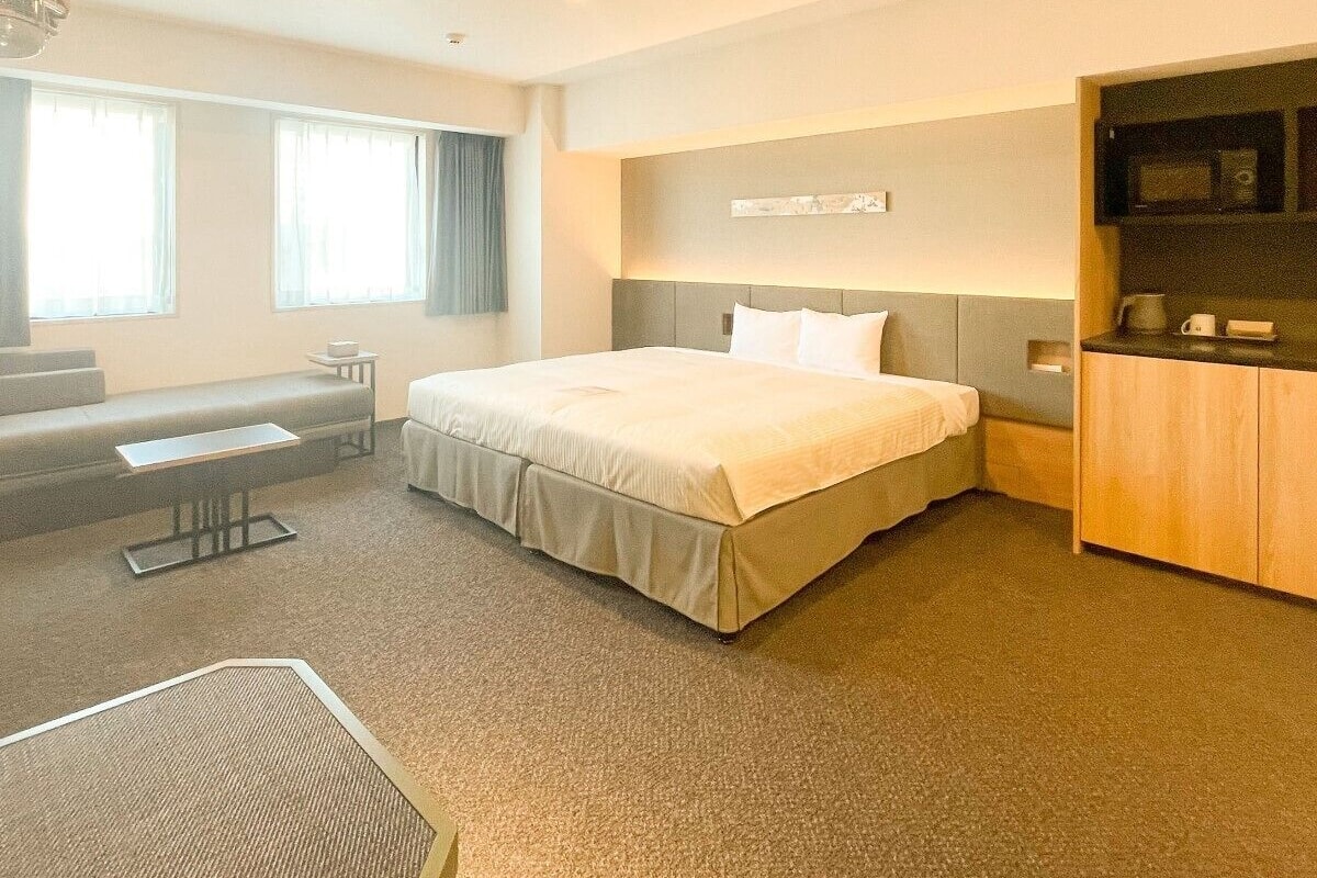 A hotel room with a bed, a desk, a chair, a microwave, and a coffee maker.
