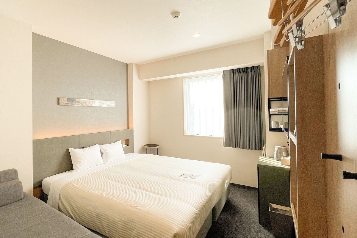 A hotel room with a large bed, a small round table, a sofa, a mirror, and a window with curtains.