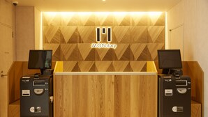 A reception desk with a geometric wood panel design and a 'MONday' logo. There are two ATMs on either side of the desk. - hotel MONday Akihabara Asakusabashi (Tokyo)