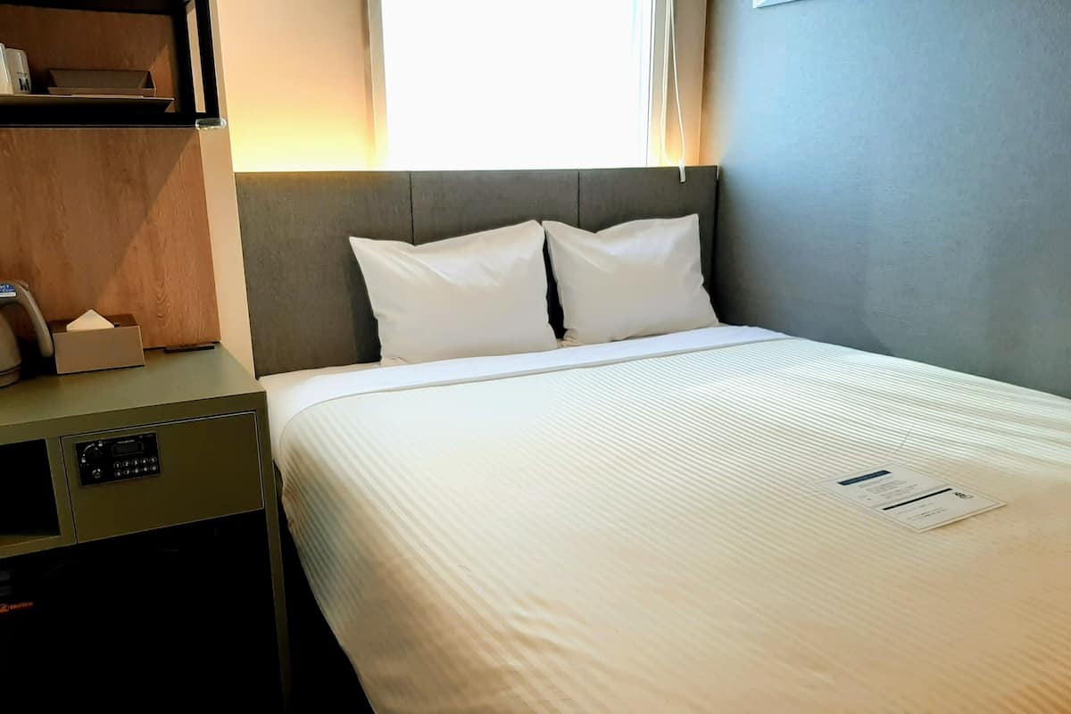A hotel room with a bed, a bedside table, and a desk with a chair.