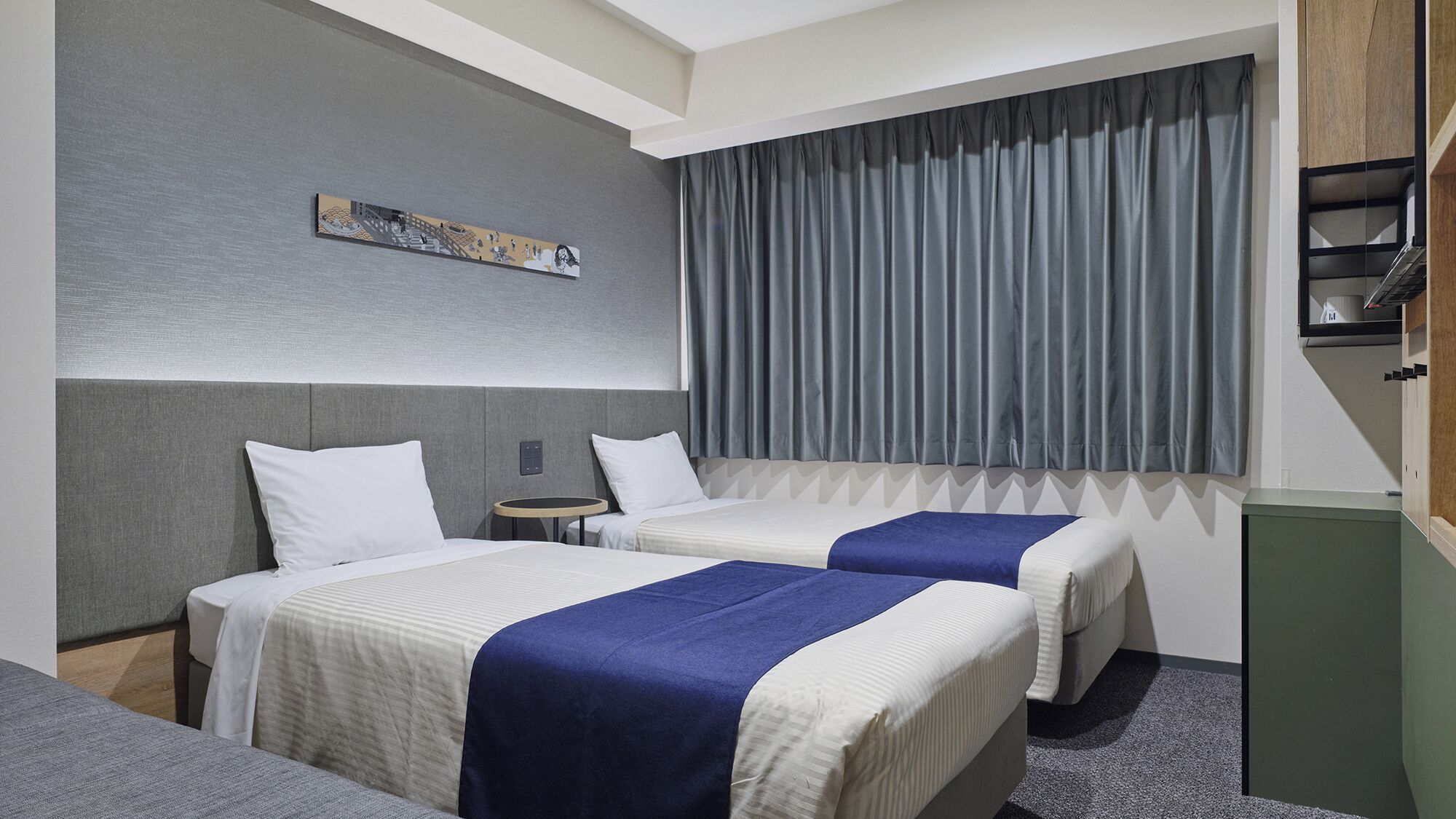 Quarto de hotel com duas camas, uma mesinha, um quadro na parede e uma janela grande com cortinas.