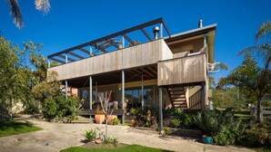 A modern house with a wooden exterior, large windows, and a covered outdoor area. - DRIFTWOOD SEVENTEEN BOOROO (Pambula Beach)
