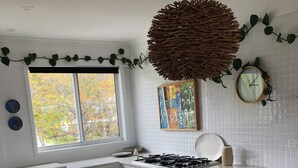 A modern kitchen with a central island, wooden stools, a gas stove, and a window with a view of trees. - DRIFTWOOD SEVENTEEN BOOROO (Pambula Beach)