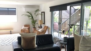 A modern living room with a black leather sofa, a wooden coffee table, and wicker chairs. - DRIFTWOOD SEVENTEEN BOOROO (Pambula Beach)