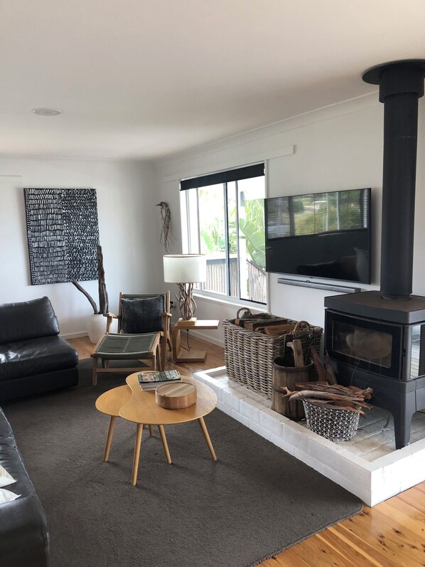 A modern living room with a black sofa, a wooden coffee table, a TV, and a wood-burning stove. - DRIFTWOOD SEVENTEEN BOOROO (Pambula Beach)