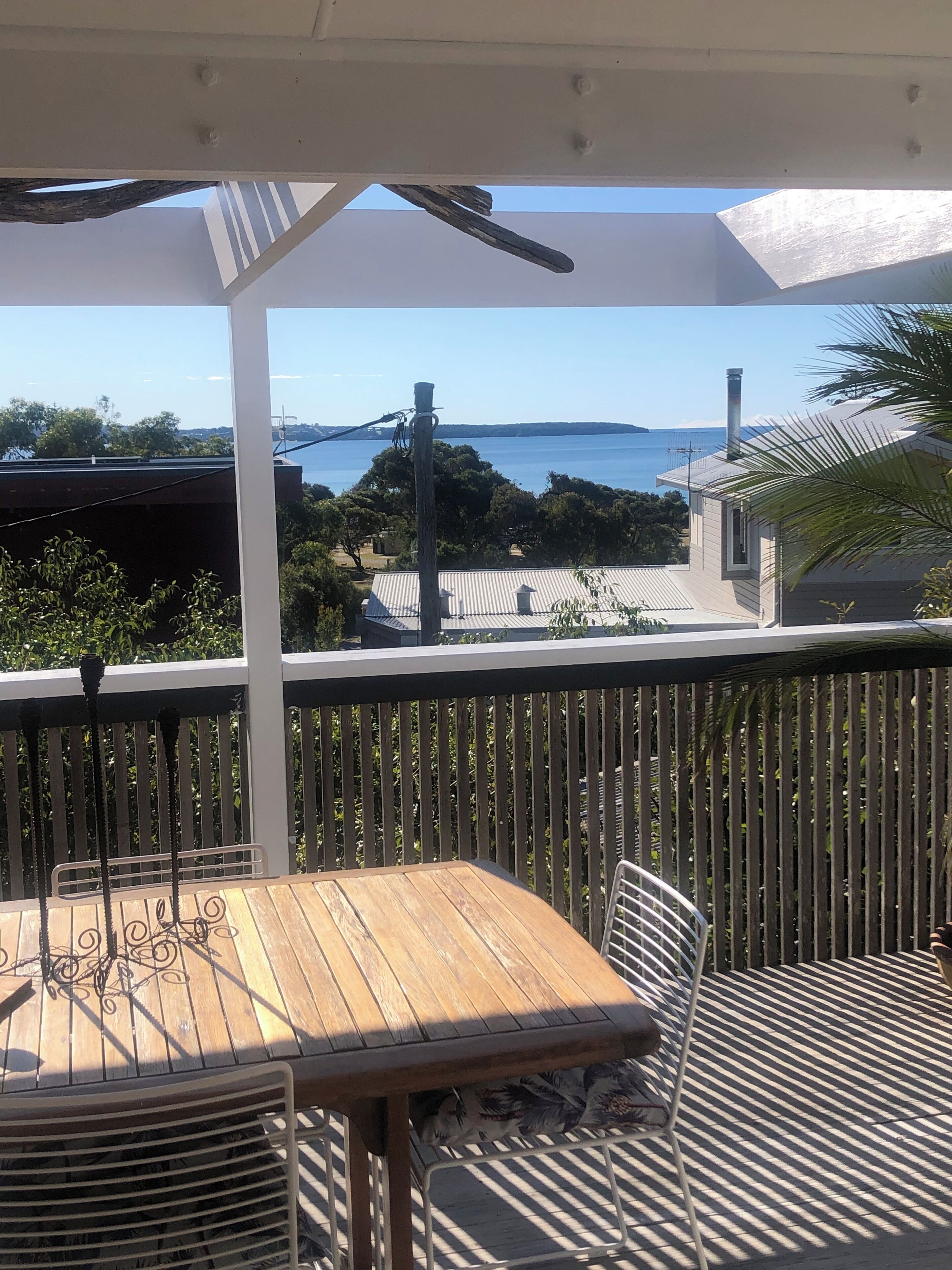 Uma mesa e cadeiras de madeira numa varanda com vista para o mar e uma ponte.