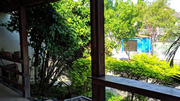 Área externa coberta com vista para um edifício azul e vegetação exuberante.