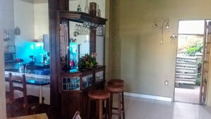 Uma área de bar com banquetas, balcão e espelho. Há uma cadeira e uma mesa em primeiro plano.