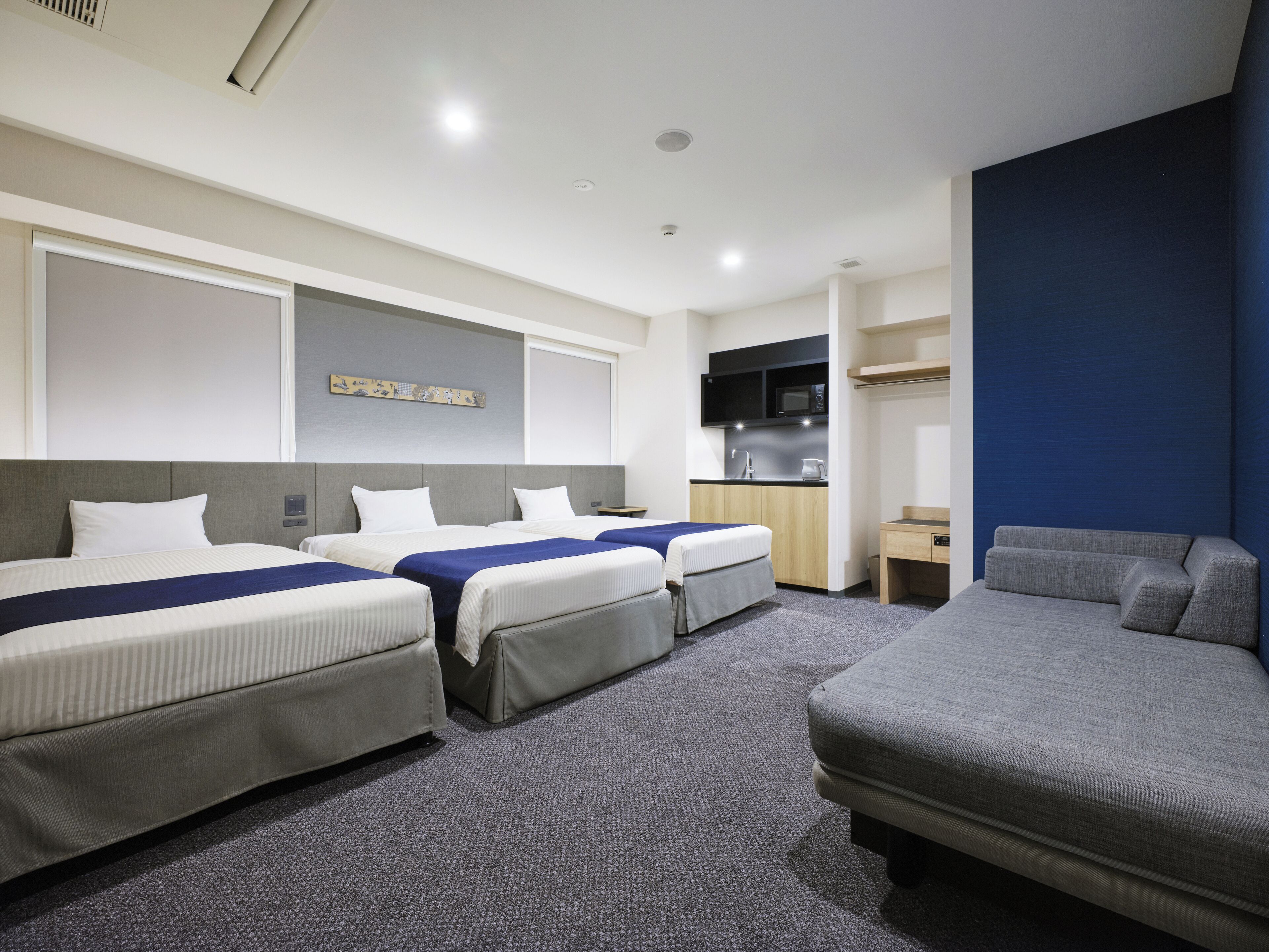 Une chambre d’hôtel avec trois lits, un canapé, une kitchenette et un téléviseur à écran plat.