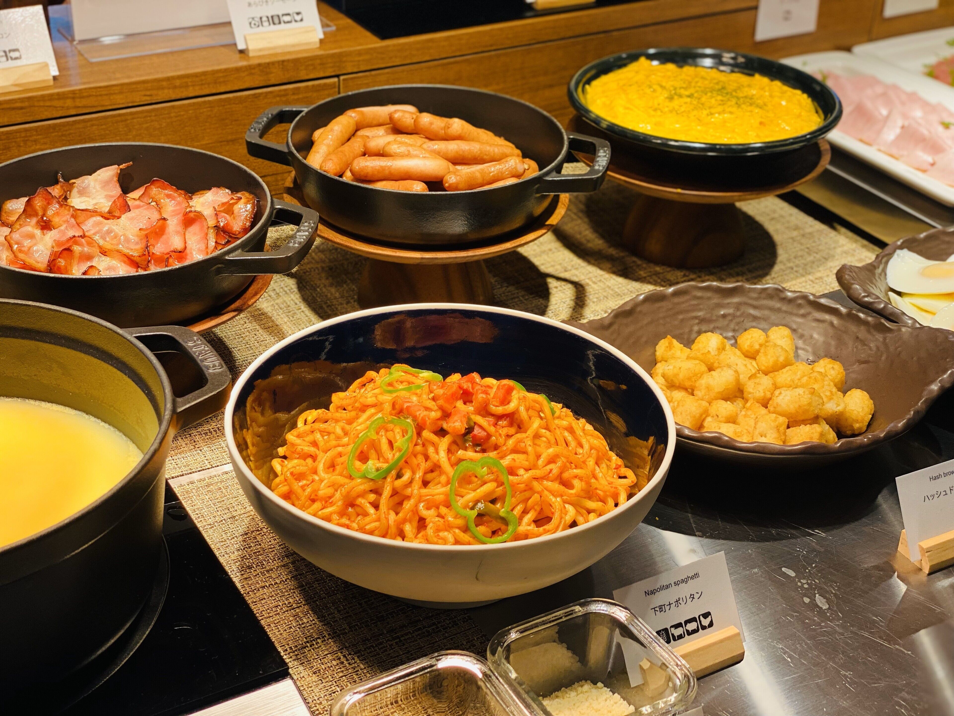 A buffet with various dishes including bacon, tater tots, and pasta.