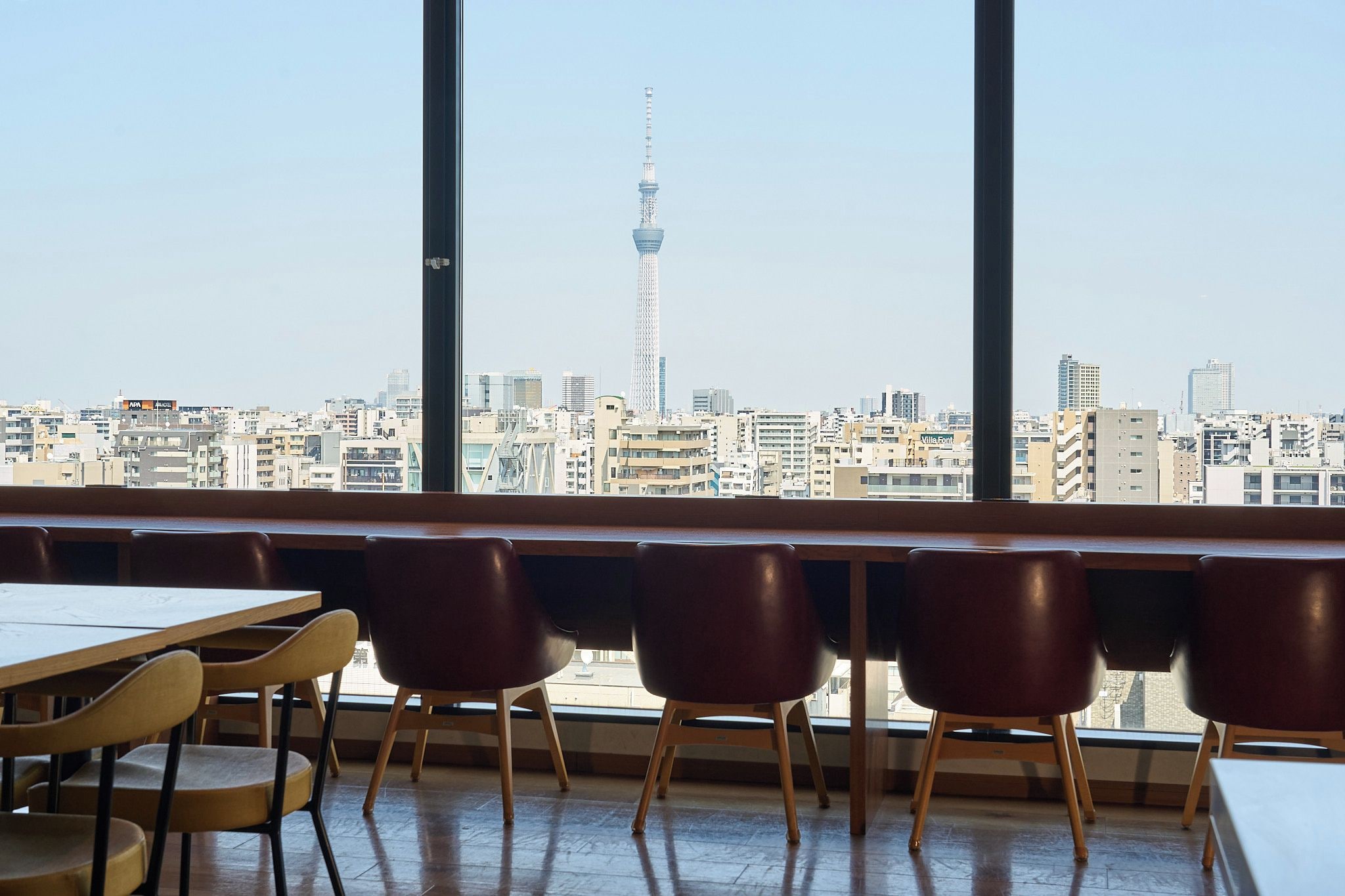 A classroom with large windows, wooden desks, and chairs, overlooking a cityscape with a prominent tower.