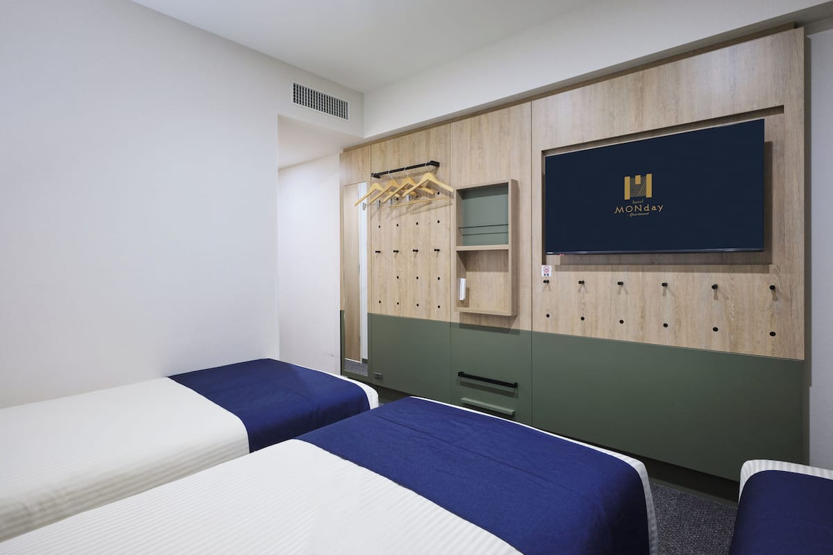 A hotel room with two beds, a wardrobe, a mirror, and a wall-mounted TV.
