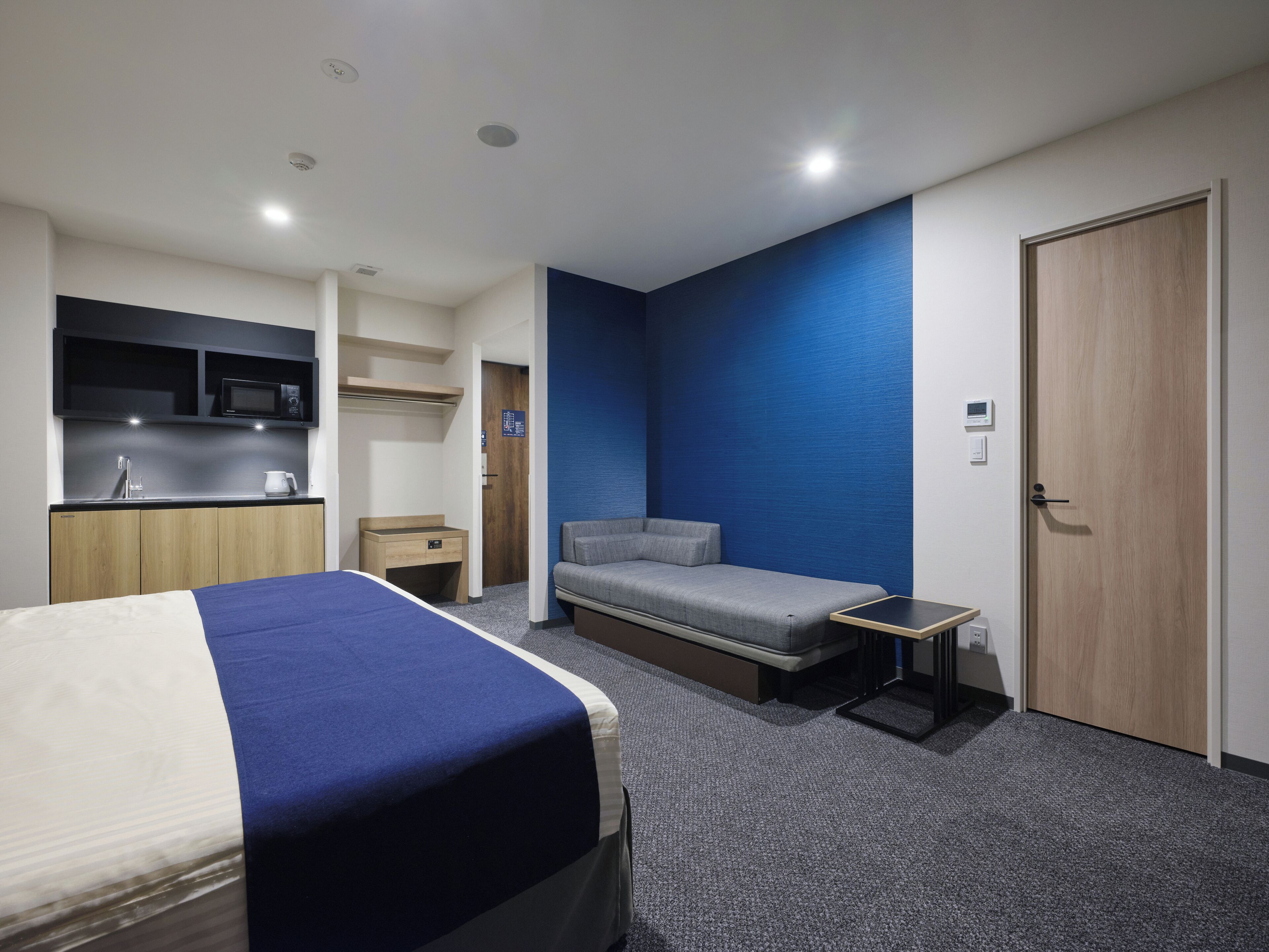Quarto de hotel moderno com uma cama, um sofá, uma pequena mesa, um micro-ondas, uma pia e um guarda-roupa.