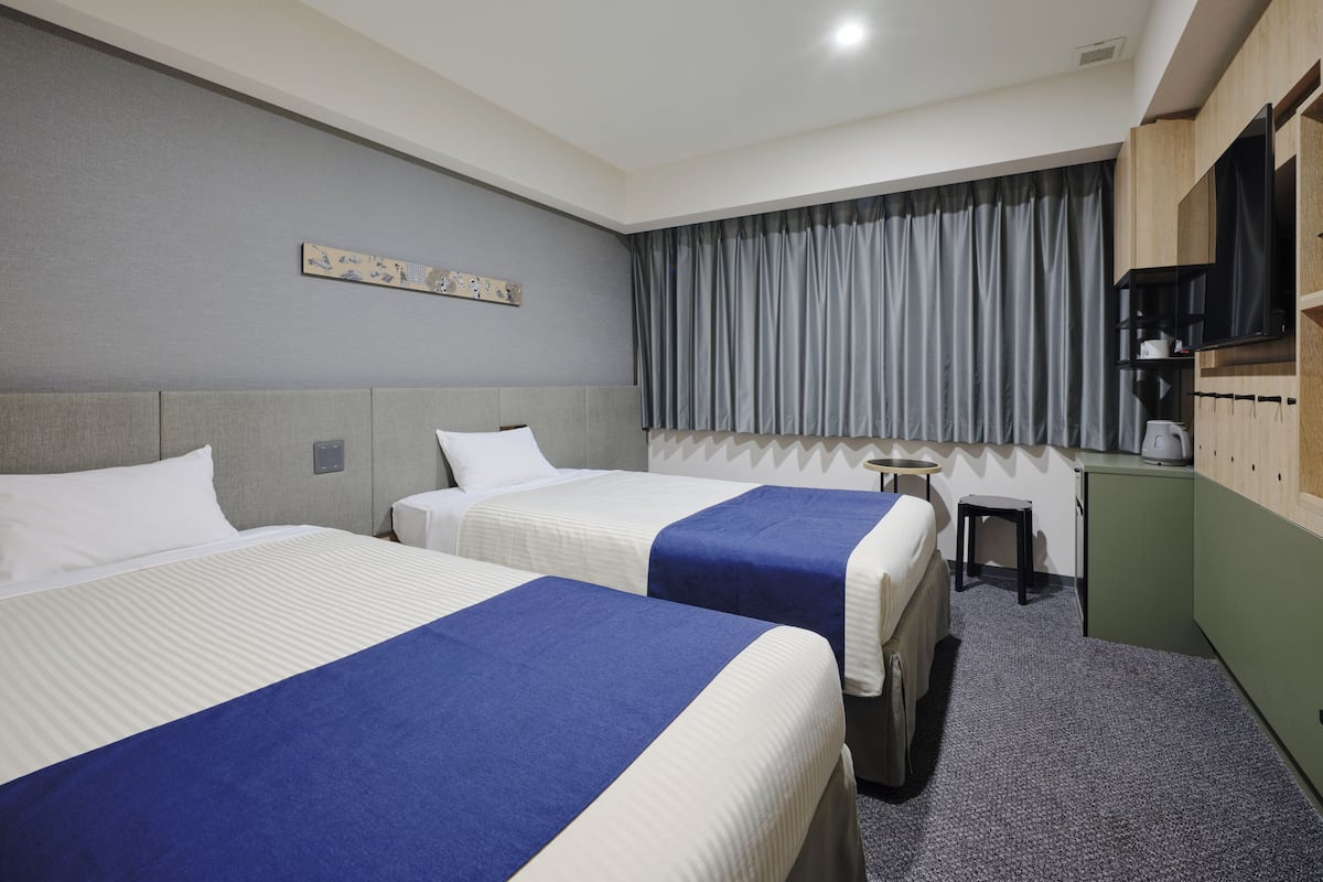 A hotel room with two beds, a small desk, a television, and a coffee machine.