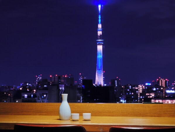 A table with a white vase and two cups, overlooking a cityscape with a lit tower at night. - hotel MONday Premium Ueno Okachimachi (Tokyo)