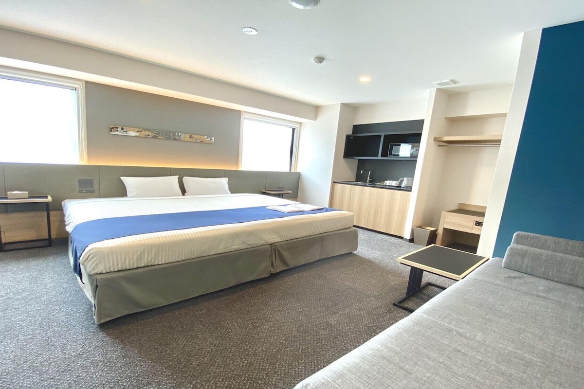 Een hotelkamer met een bed, een slaapbank, een bureau, een televisie en een kitchenette.