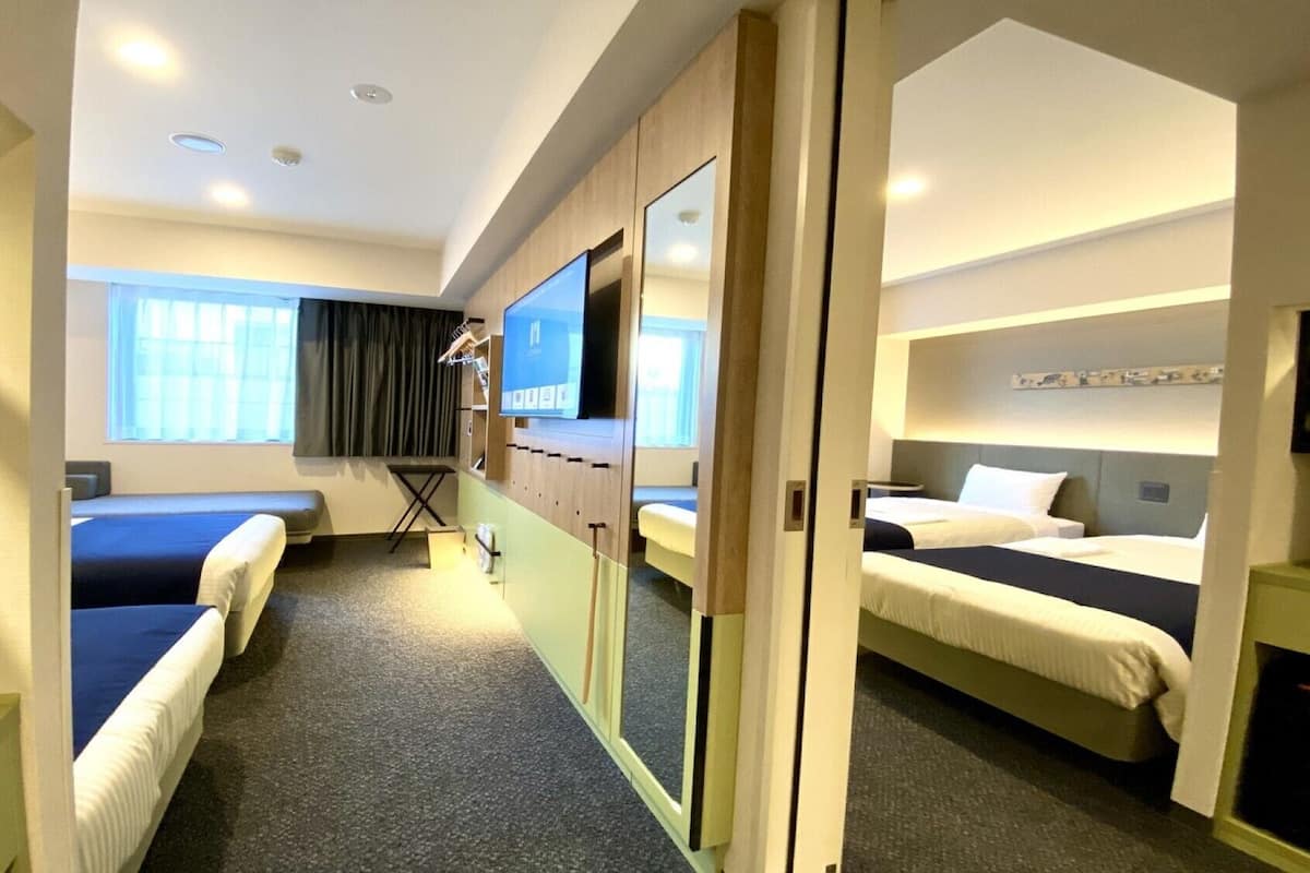A hotel room with two beds, a TV, a desk, and a window.