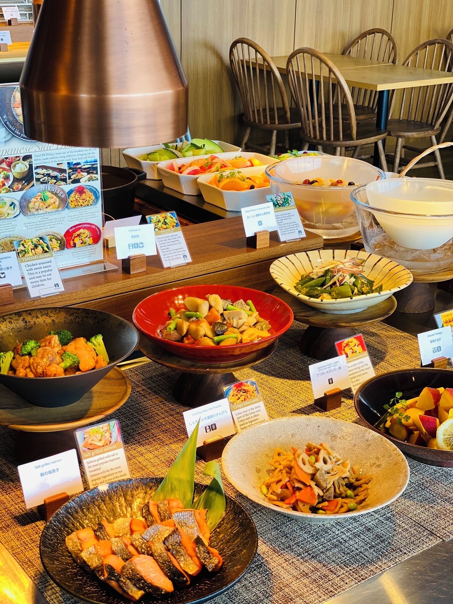 A variety of dishes on a buffet table with labels and a menu stand.