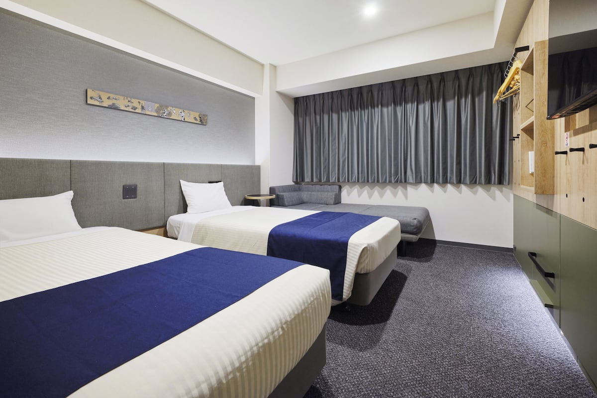 A hotel room with two beds, a flat-screen TV, a coat rack, and a large window with curtains.