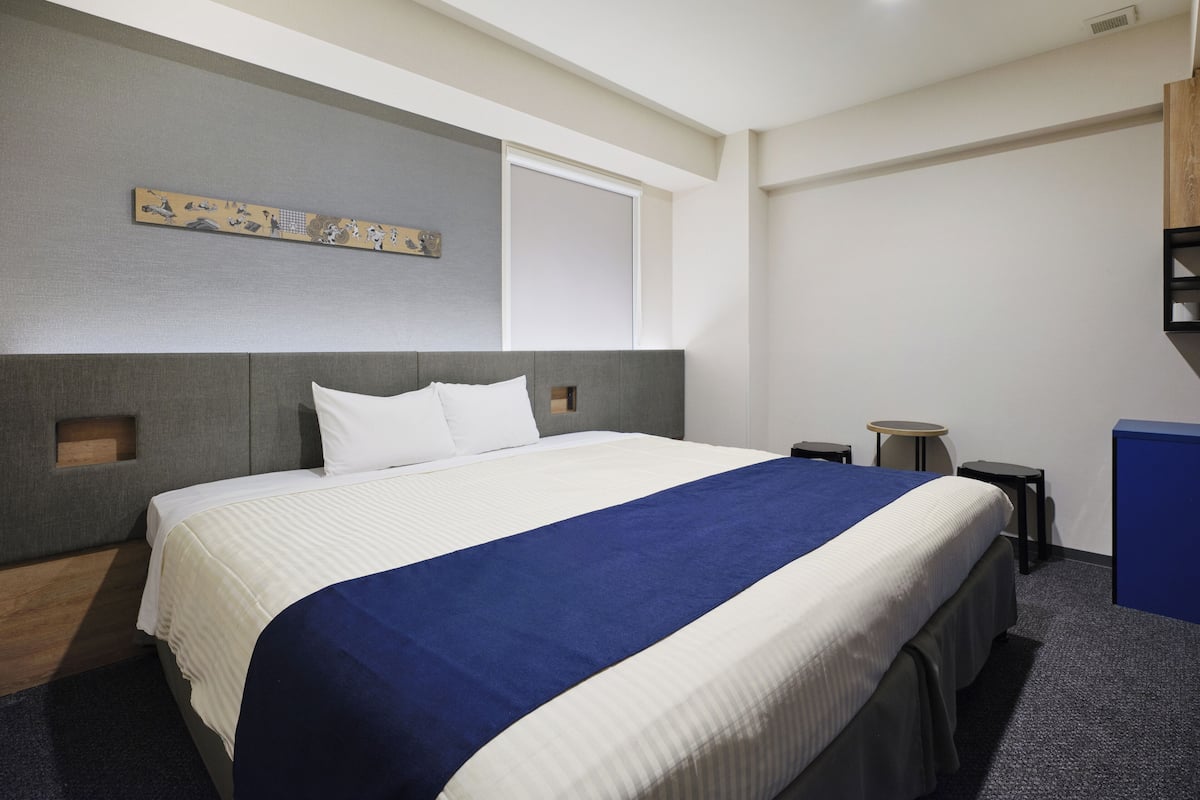A modern hotel room with a large bed, a small desk, and a window.