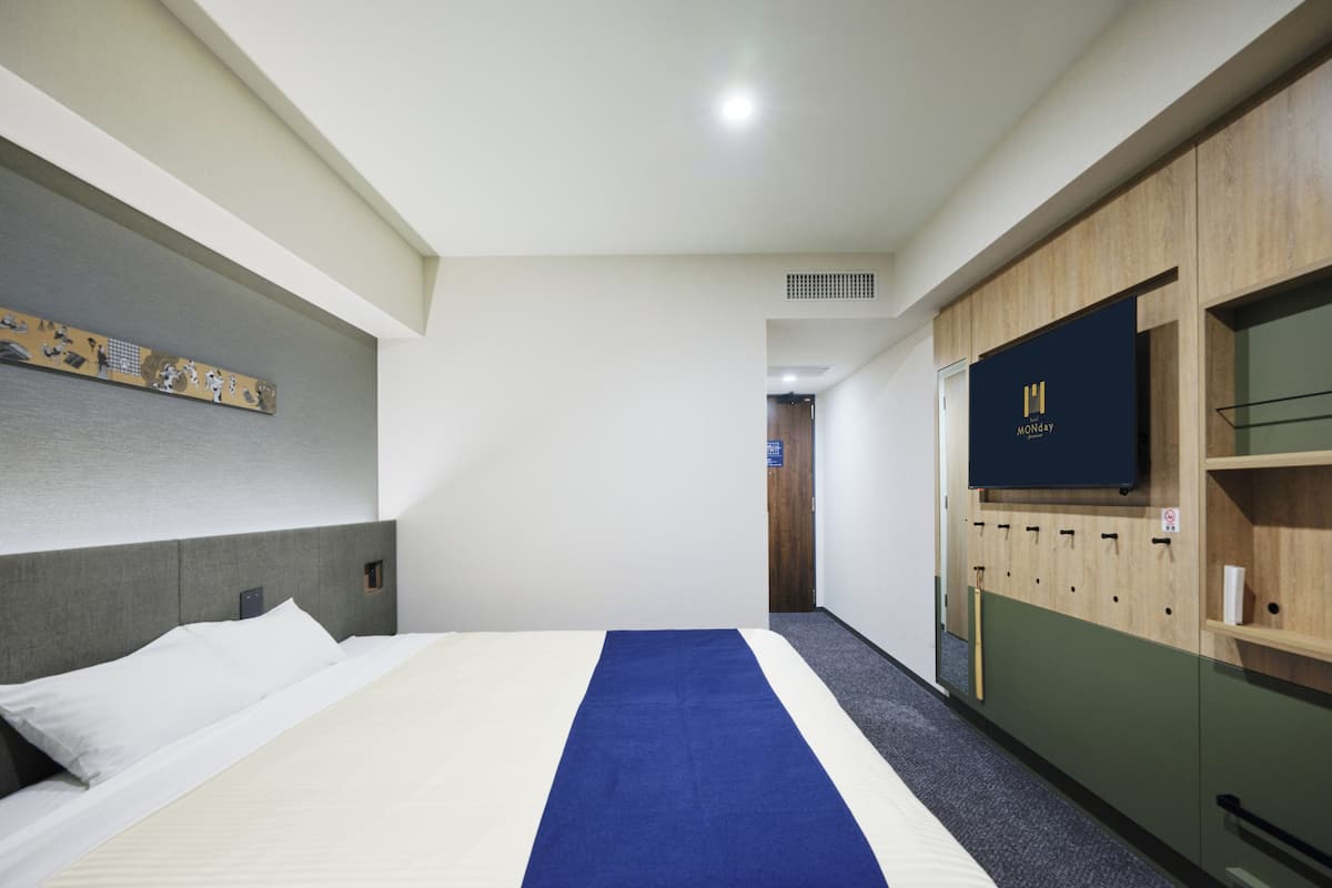 A hotel room with a bed, a TV, a wardrobe, and a door leading to another room.