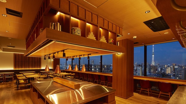 A modern restaurant with a high ceiling, wooden paneling, and a view of a cityscape. - hotel MONday Premium Ueno Okachimachi (Tokyo)