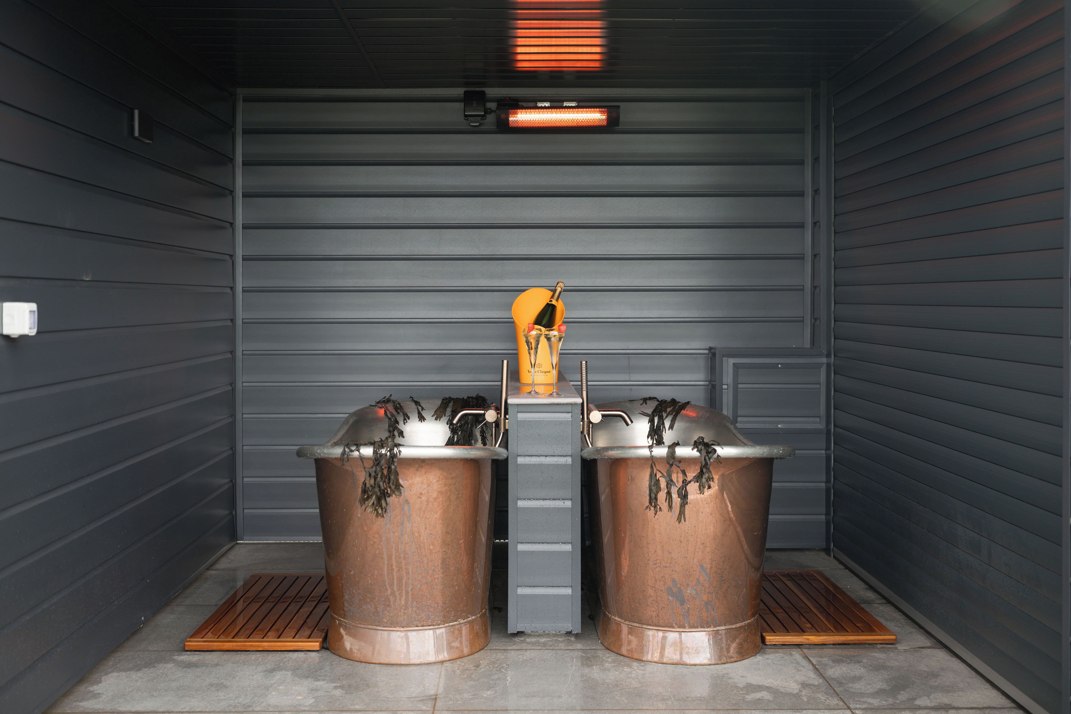 A room with two copper sinks, a bottle of champagne, and a heater.