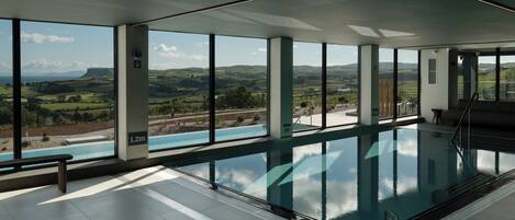 Une piscine intérieure moderne, dotée de grandes fenêtres offrant une vue sur un paysage verdoyant.