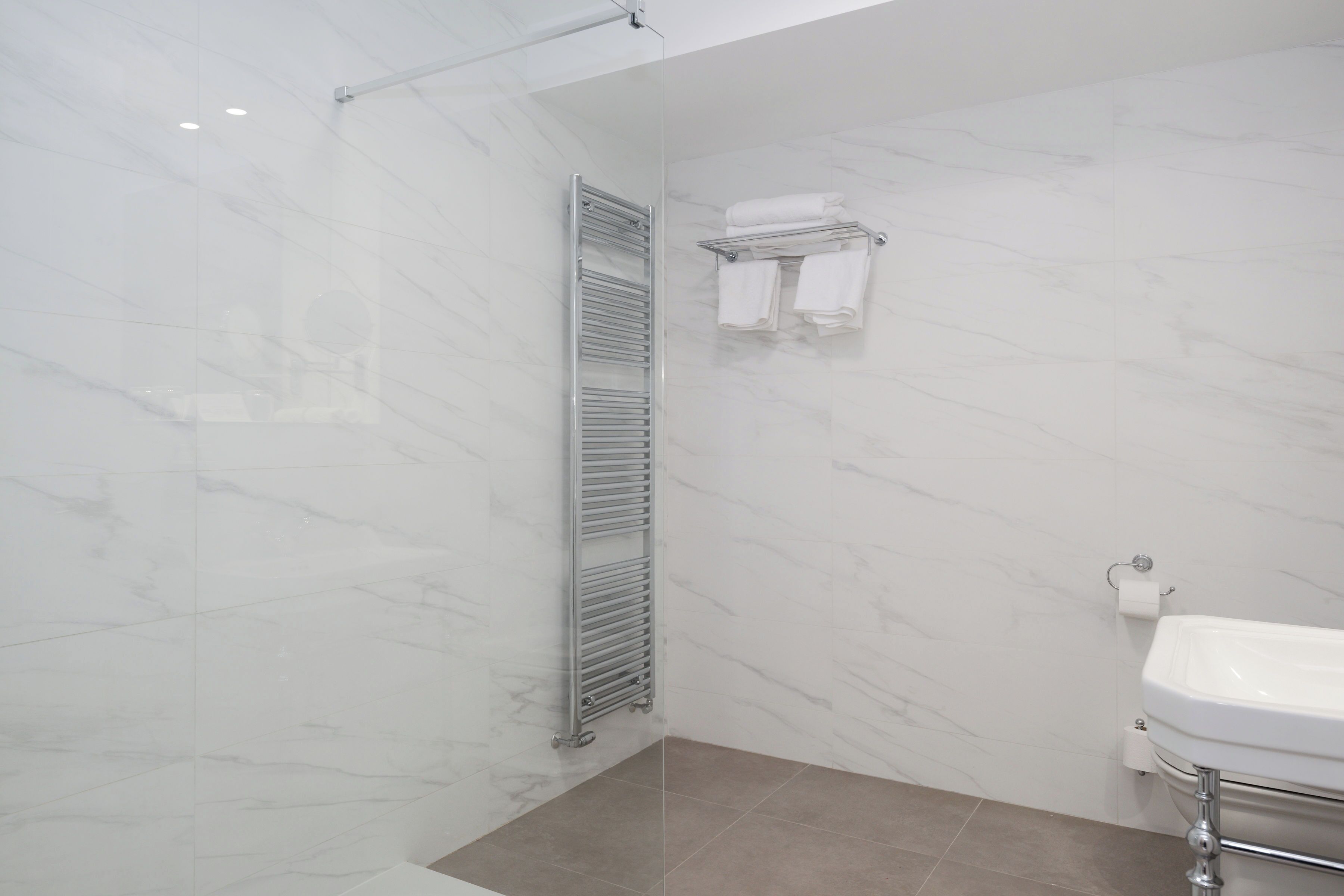 A modern bathroom with a glass shower enclosure, a built-in towel rack, and a white sink.