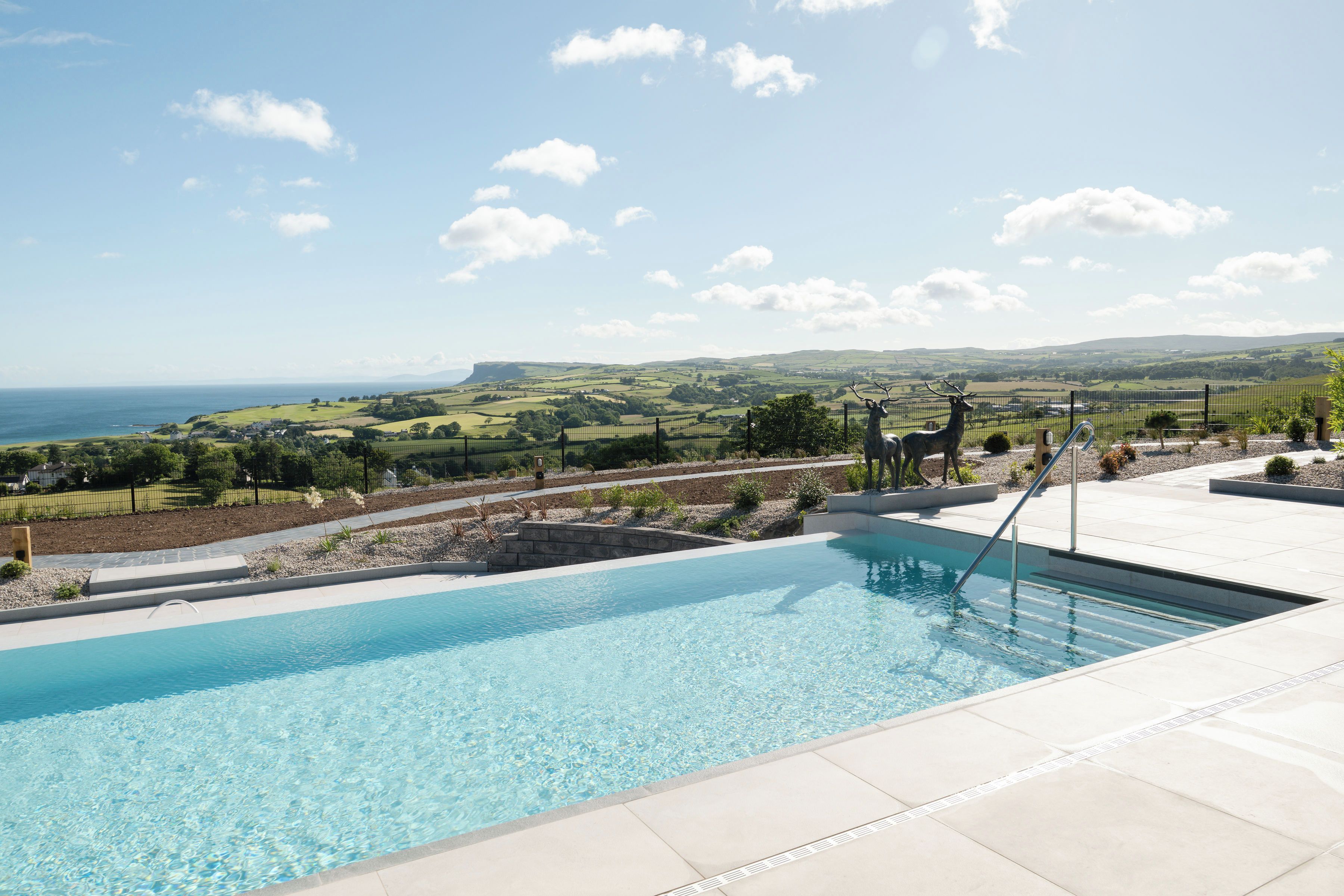 A swimming pool with a view of the sea and rolling hills in the background.