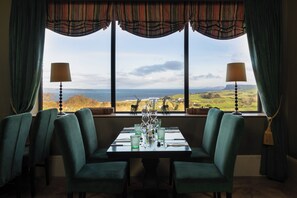 A dining area with a table set for four, two lamps, and a view of the countryside through large windows. - The Salthouse Hotel (Ballycastle)