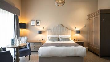 A hotel room with a large bed, bedside lamps, a chandelier, a desk with a chair, and a wardrobe.