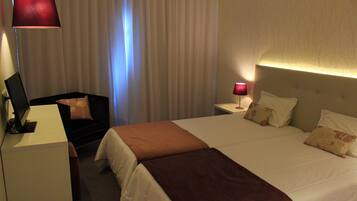 A hotel room with a bed, a desk, a chair, and a lamp.