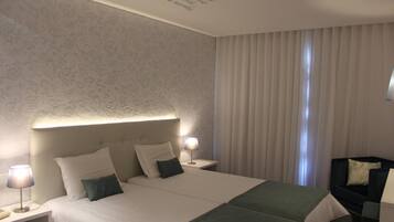 A hotel room with a large bed, a nightstand with a lamp, a chair, and a window with curtains.