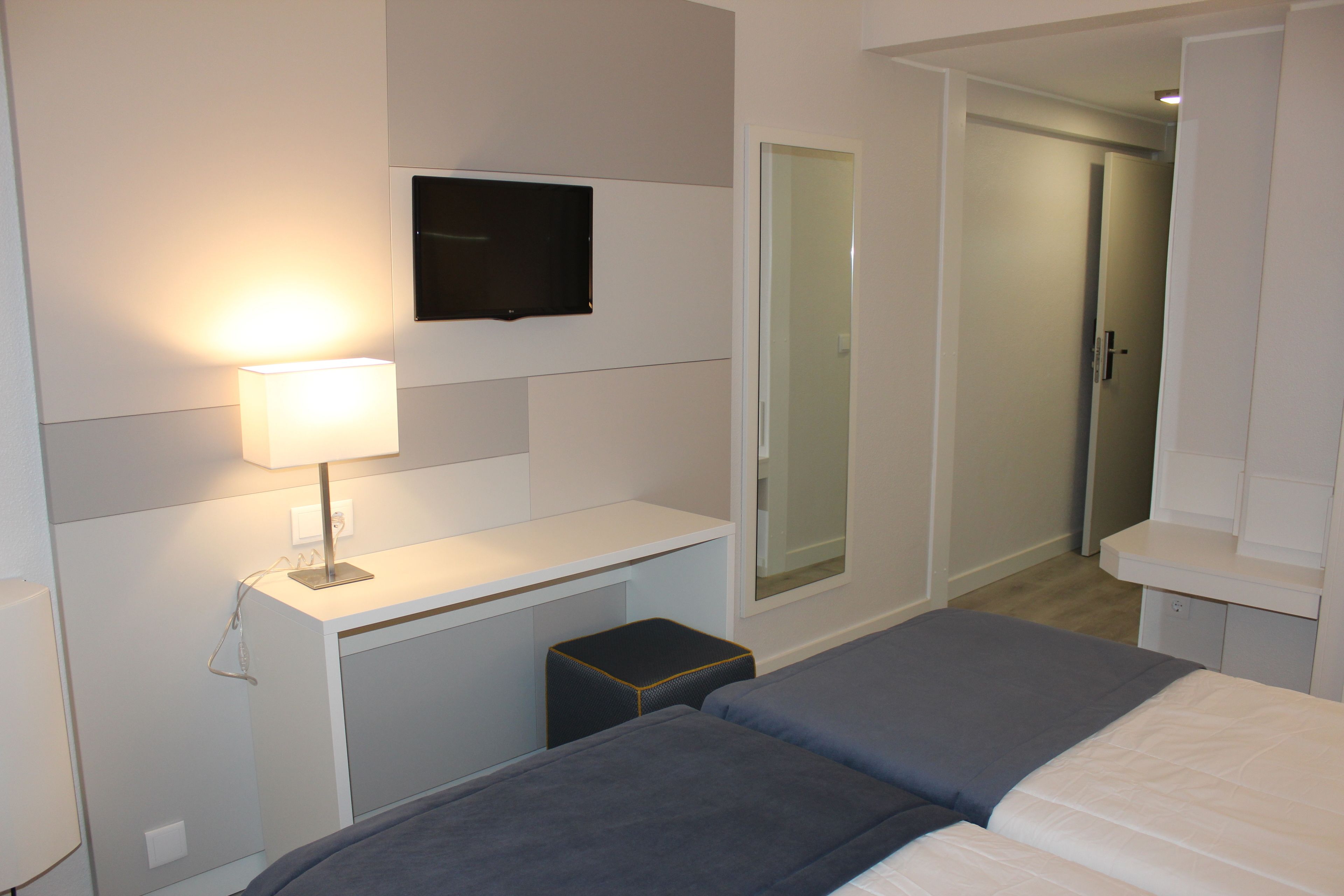 Una habitación de hotel con cama, mesita de noche, lámpara, televisor y espejo.