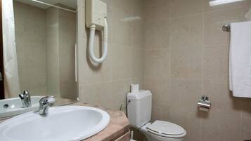 A bathroom with a sink, mirror, toilet, and a hand dryer.