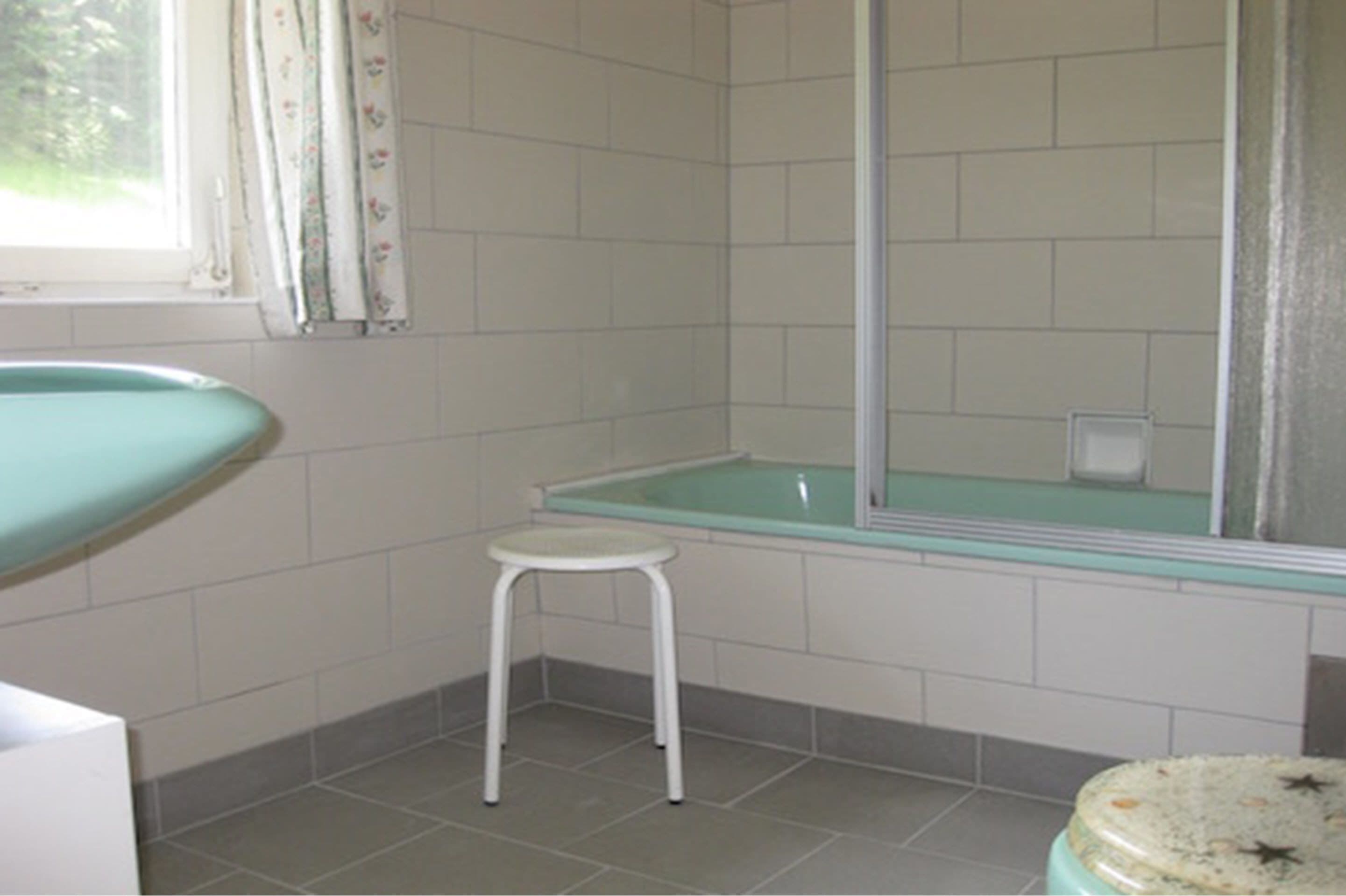 A bathroom with a bathtub, a small stool, and a toilet.