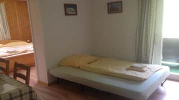 Quarto com cama, um banco e uma mesa. Duas molduras com quadros na parede.