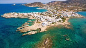 An aerial view of a coastal town with white buildings, clear blue waters, and rocky terrain. - Domus Litus (Milos)