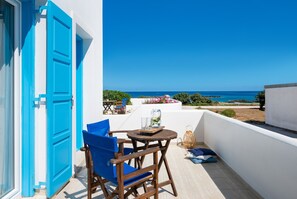 Un balcón con vistas al mar, una mesa de madera con sillas y una puerta azul.