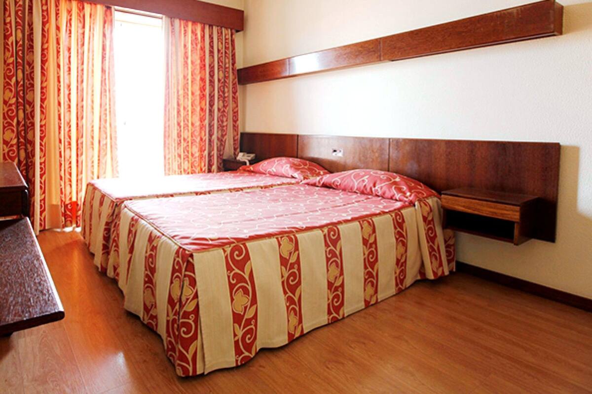 Una cama doble con colcha estampada, cabecera de madera y mesita de noche con lámpara.