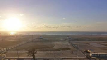 A parking lot with a few cars, a clear sky, and a distant view of the ocean.