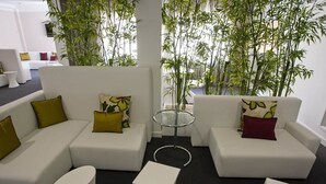 Een moderne woonkamer met witte banken, groene en rode kussens, een glazen salontafel en bamboeplanten.