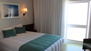 Een hotelkamer met een bed, nachtkastje, lamp, raam met gordijnen en uitzicht op de omgeving.