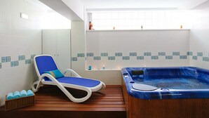 Een spa-ruimte met een houten vloer, een blauwe fauteuil, een whirlpool en een raam met uitzicht op de lucht.