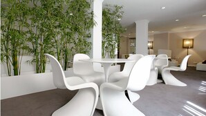 Een modern interieur met een ronde tafel, omringd door witte stoelen, een grote potplant en een bank.