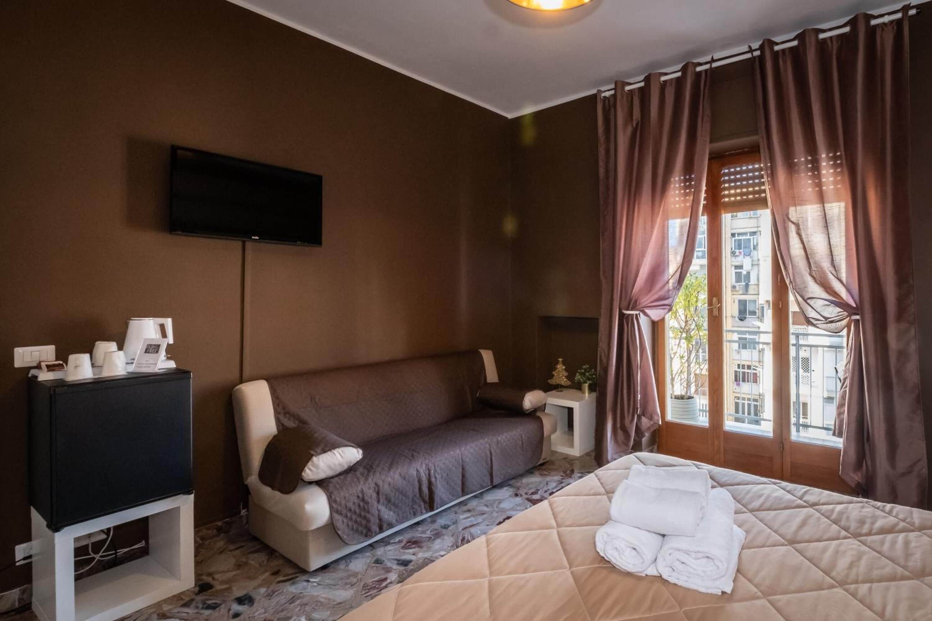 Ein Hotelzimmer mit Bett, Sofa, Fernseher und einem Fenster mit Vorhängen.