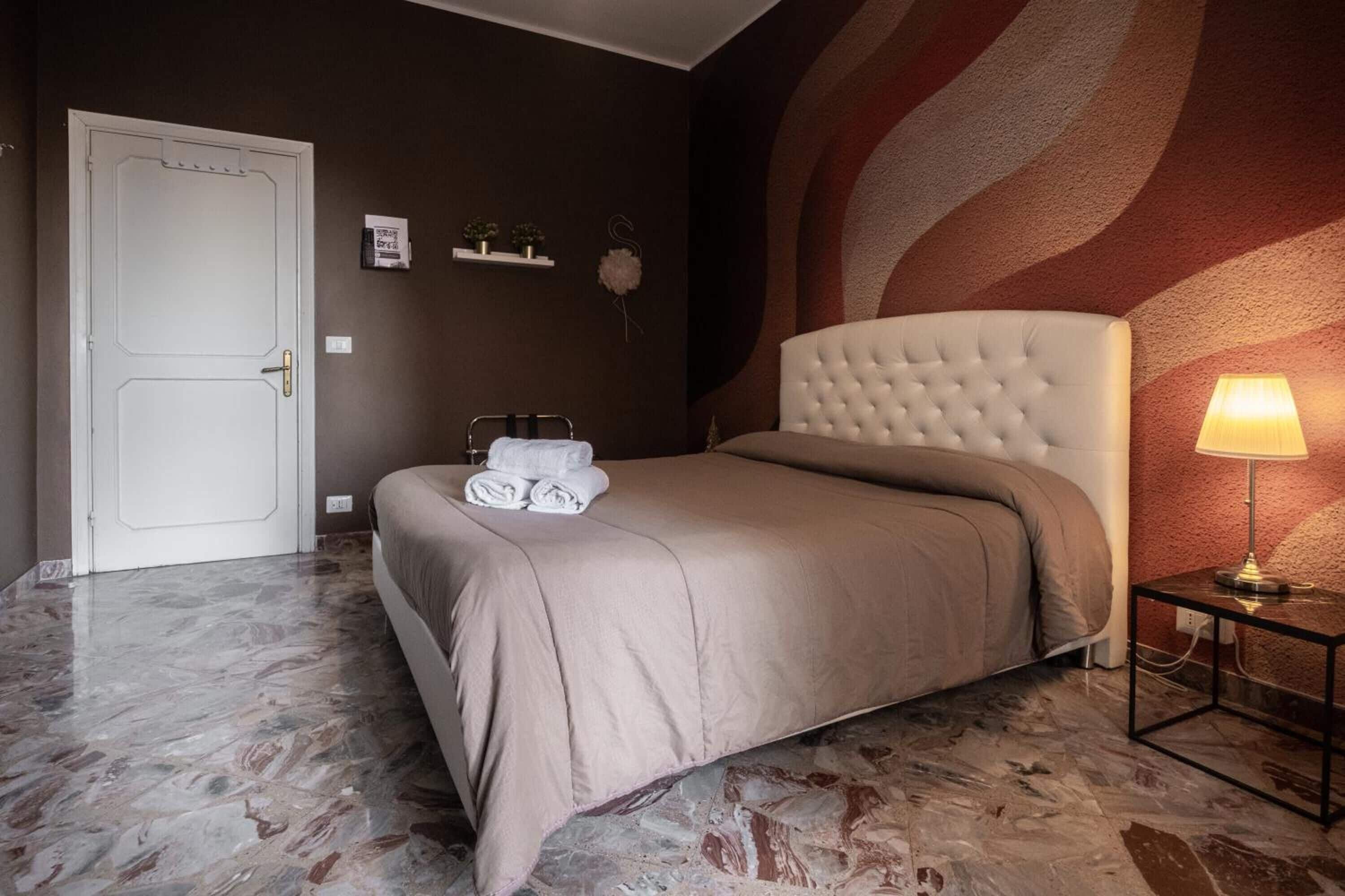 Habitación de hotel con piso de mármol, cama con cubrecama color beige, lámpara de noche y pared con diseño texturizado.