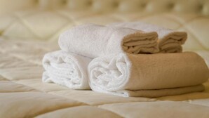 Una toalla blanca doblada con cuidado y una toalla beige apiladas sobre una cama con una colcha blanca texturizada.